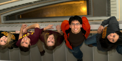 a group of five people arch their backs to look up a steep stairwell to where the camera is located